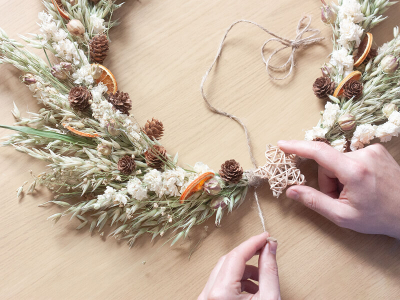 A close up of a person making a dried seasonal wreath at a Crafty Hen workshop